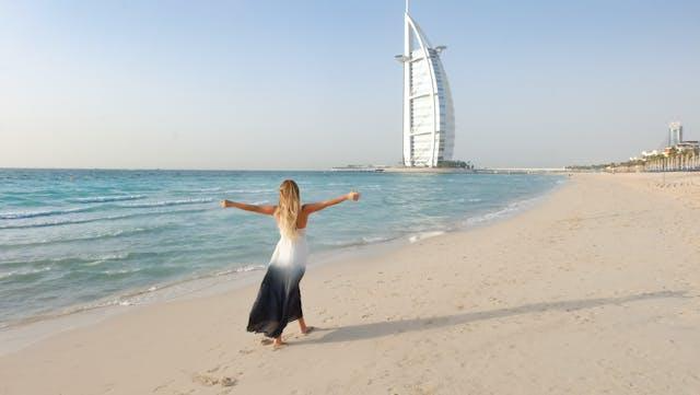 A woman in a black-and-white dress spreading her hands on a Dubai beach.