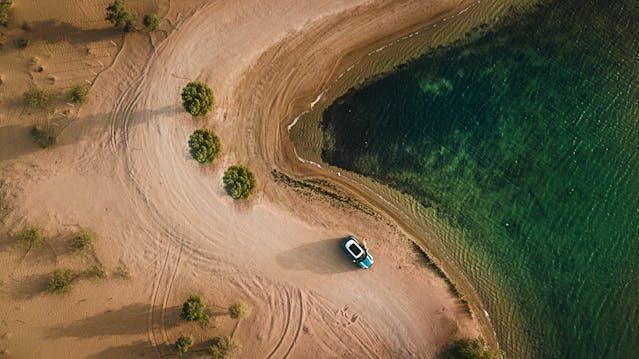 A top-down view of a car parked along a desert road, near the shore.